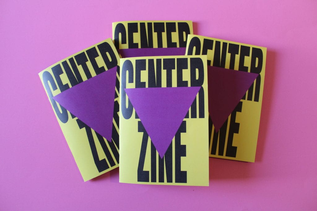 4 copies of Centre zine sit on top of a pink surface. The zine has a bright yellow cover with the words Centre Zine in bold capitalised typeface covering the whole page. A big, purple triangle sits on top of the text.