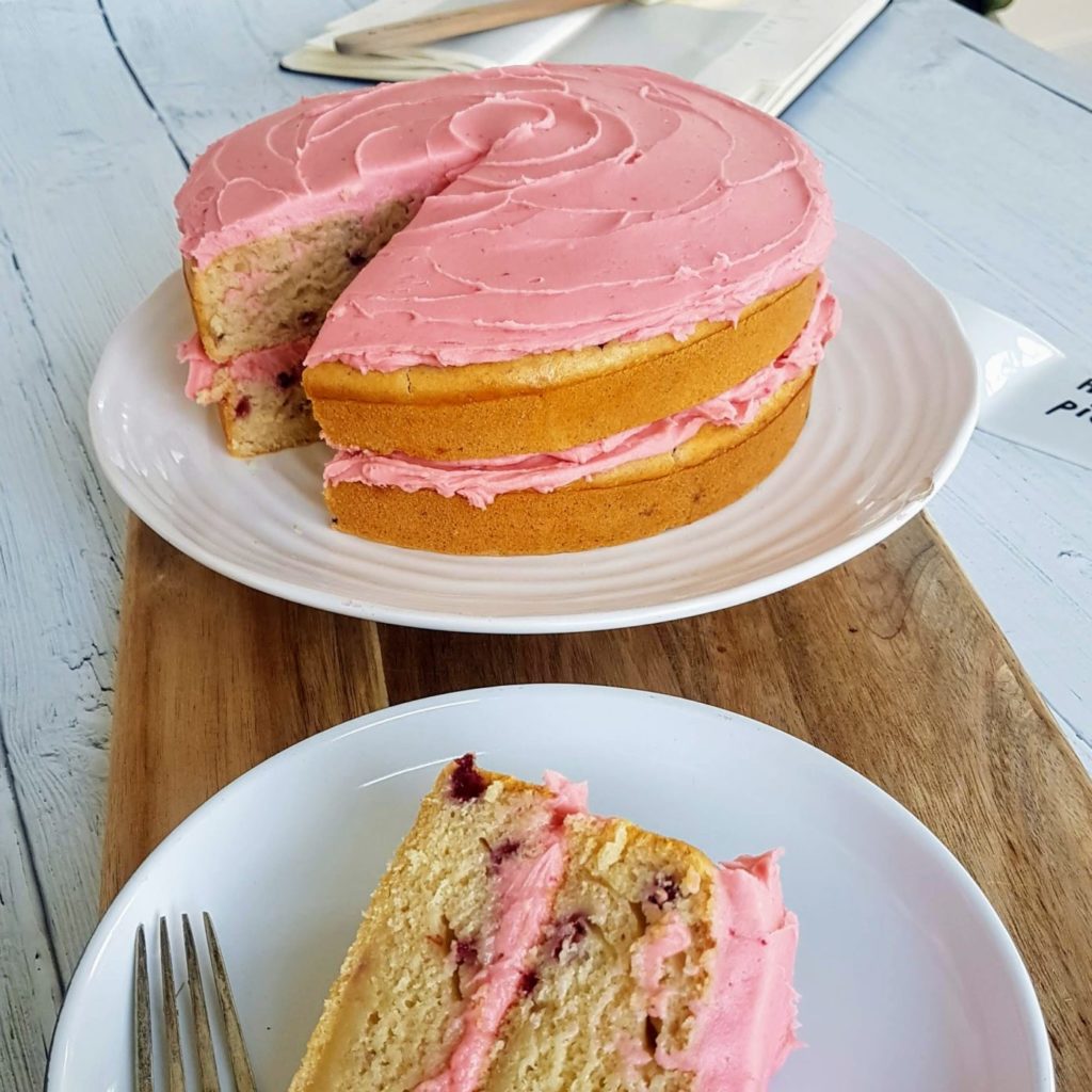 A vegan cake with pink icing sits sliced and ready to eat.