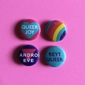 4 badges. The badges say, Andro and Eve, Reyt Queer, and Queer Joy. The fourth badge is a 5 stripe rainbow.