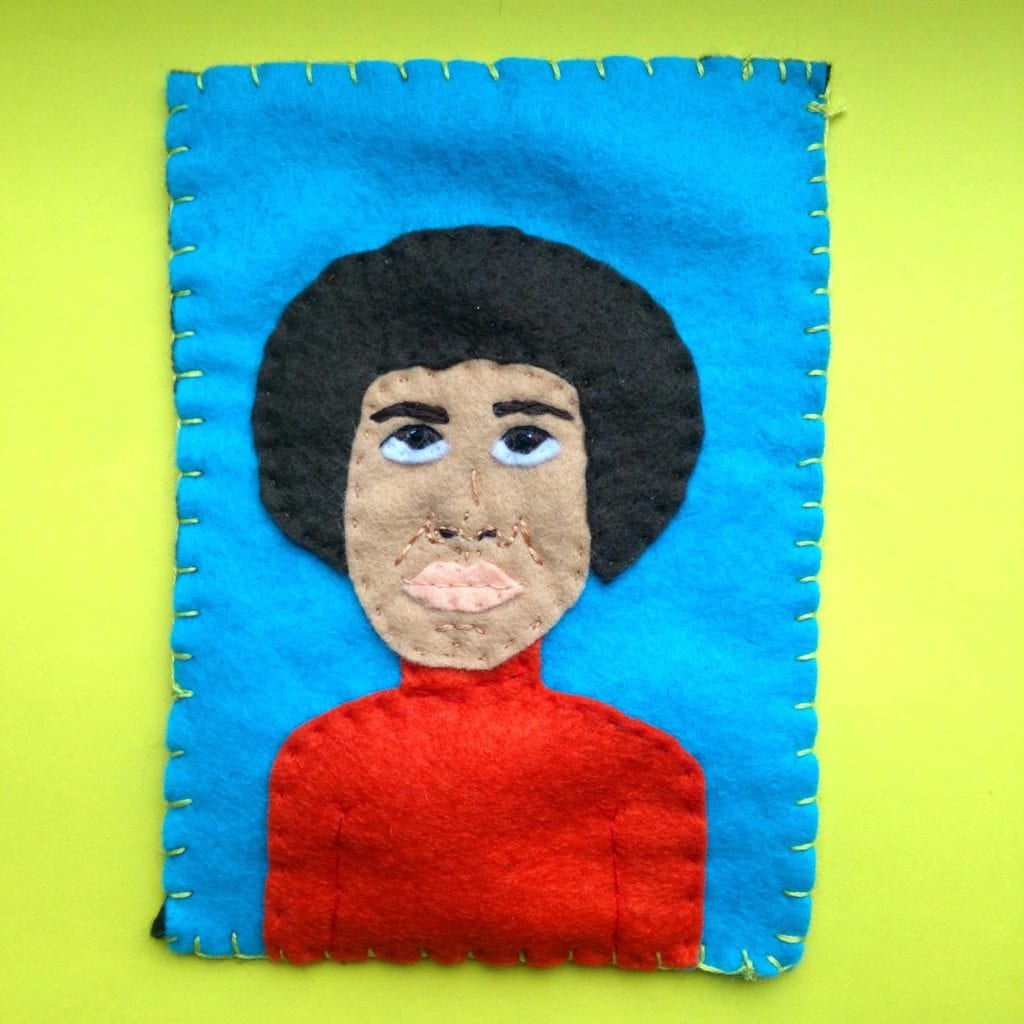 A felt portrait of Angela Davis. She is wearing a red polo neck and has a net afro hairstyle. 