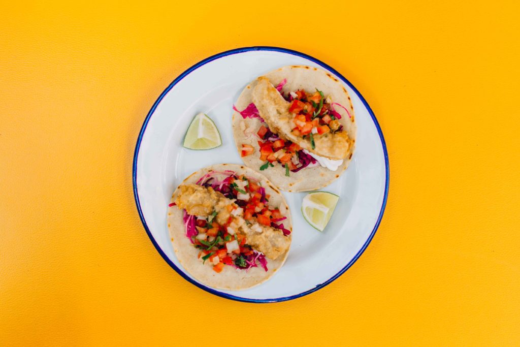 a plate of fresh tacos sits on a white plate with blue rim on a yellow table