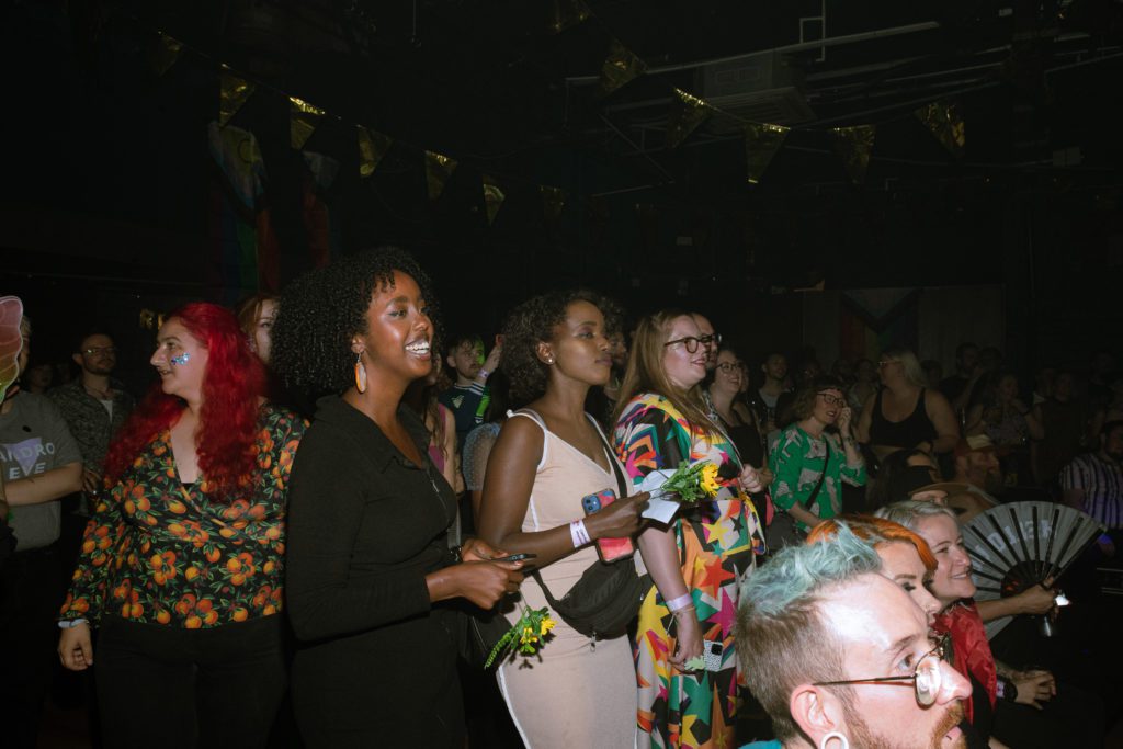 a crowd of people in a dark room look upon a stage out of shot