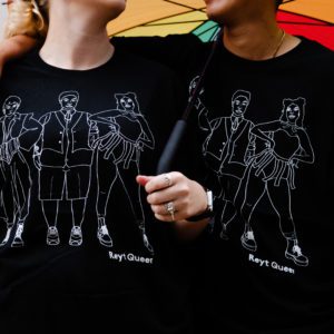 Two people, one white and one brown stand side by side modelling a black tee with a linework illustration of three figures in white