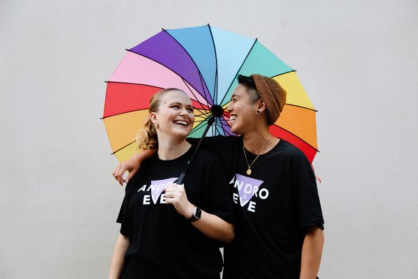 two peoplesmiling wearing Andro and Eve logo tee holding a rainbow umbrella