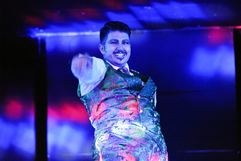 drag king Mark Anthony onstage smiling with sparkly eyebrows and brocade suit