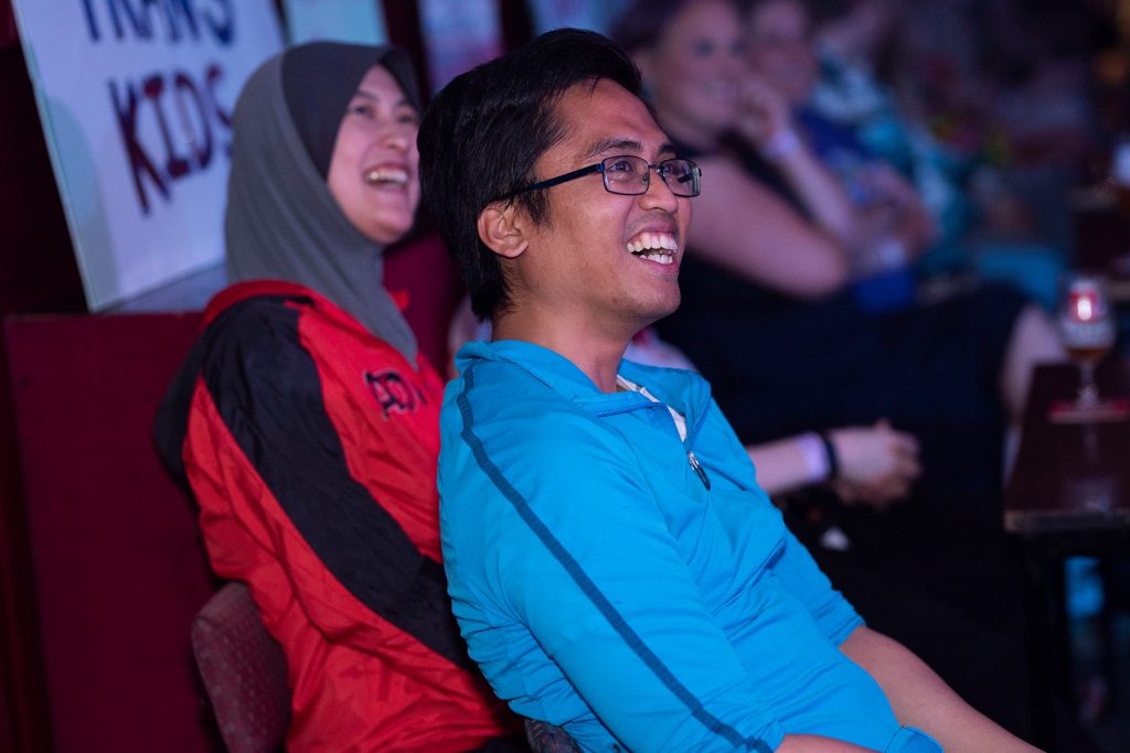 Two South East Asian people smile with open mouths up at the stage. The woman is wearing a headscarf