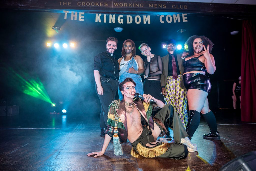 Drag king Richard Energy sits on stage flanked by kings, Shardeazy Afrodesiak, Unknown Amazon, Toby Carvery, Wesley Dykes and Billy Butch