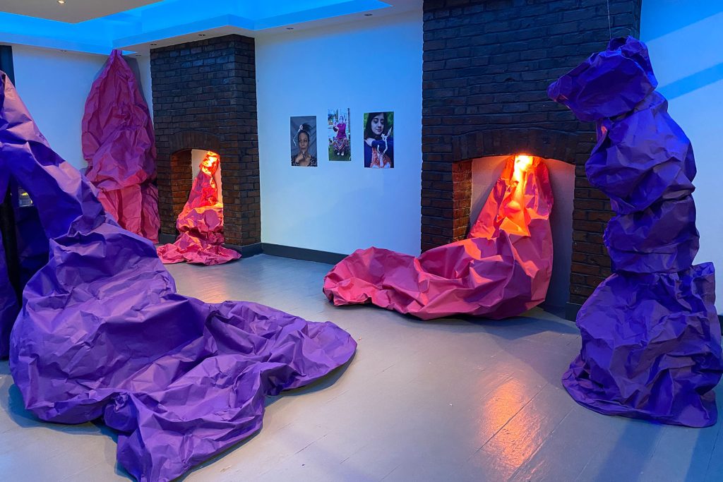 An installation which includes giant paper sculptures made from 11meter by 2.75 meter sheets of bright pink and purple, recycled paper. The sculptural works are lit from outside, and within, by a variety of lights in shades of blue and white