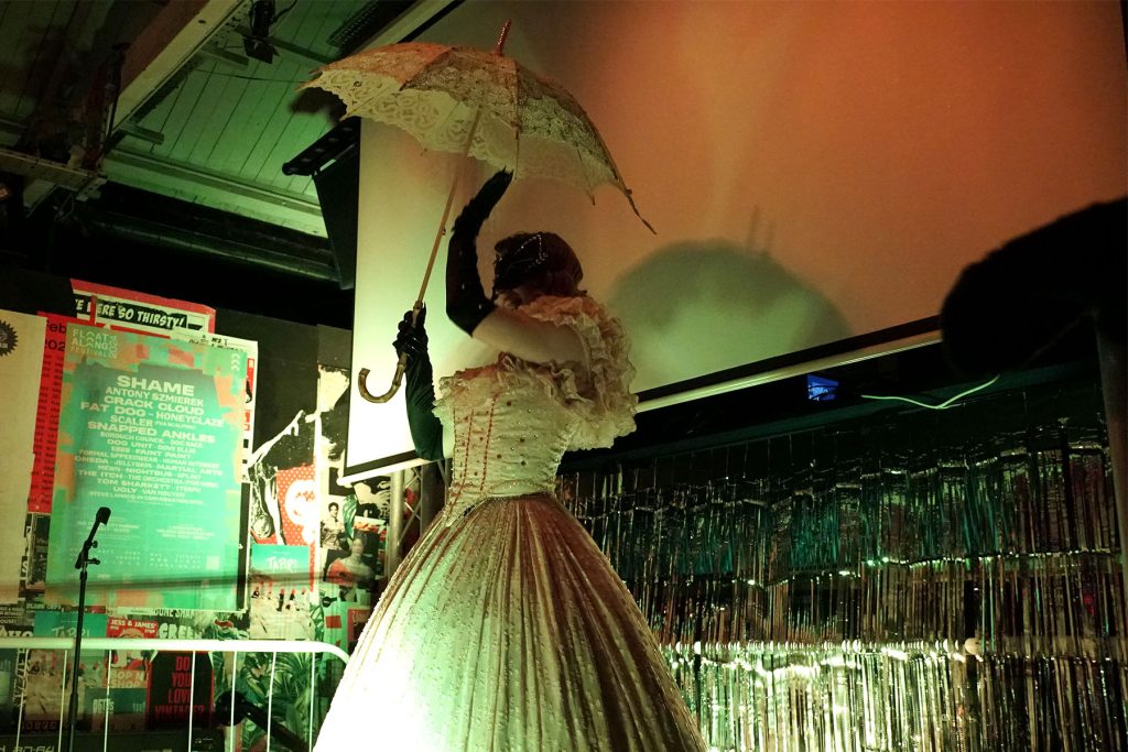 Burlesque artist Sphynxie holds an umbrella high onstage while she performs