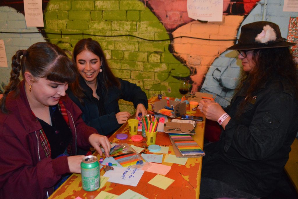 Three people craft with modelling clay at a table in a brightly painted courtyard