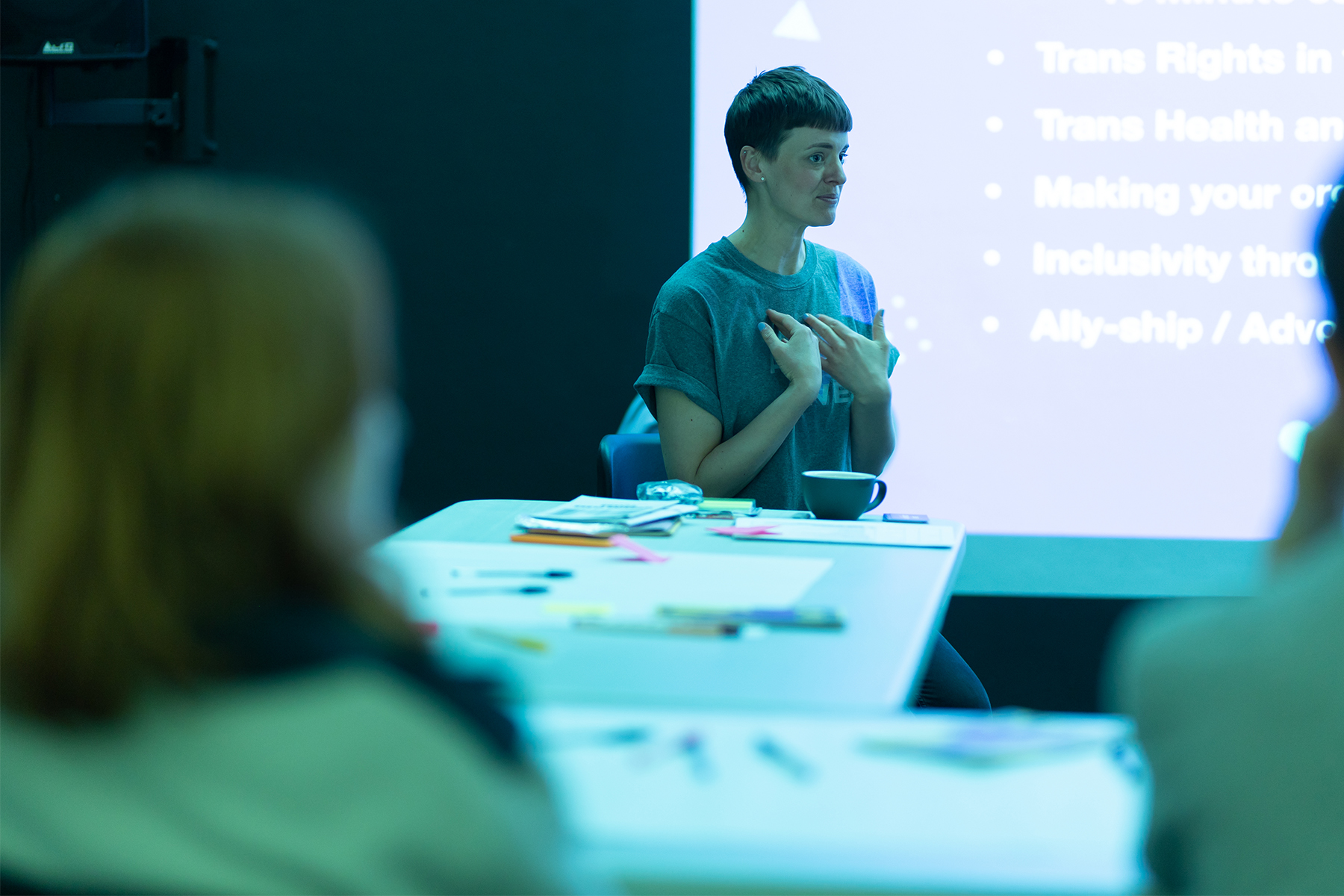 Finn, a slim androgynous person with short brown hair sits in front of a screen presenting to a group of people