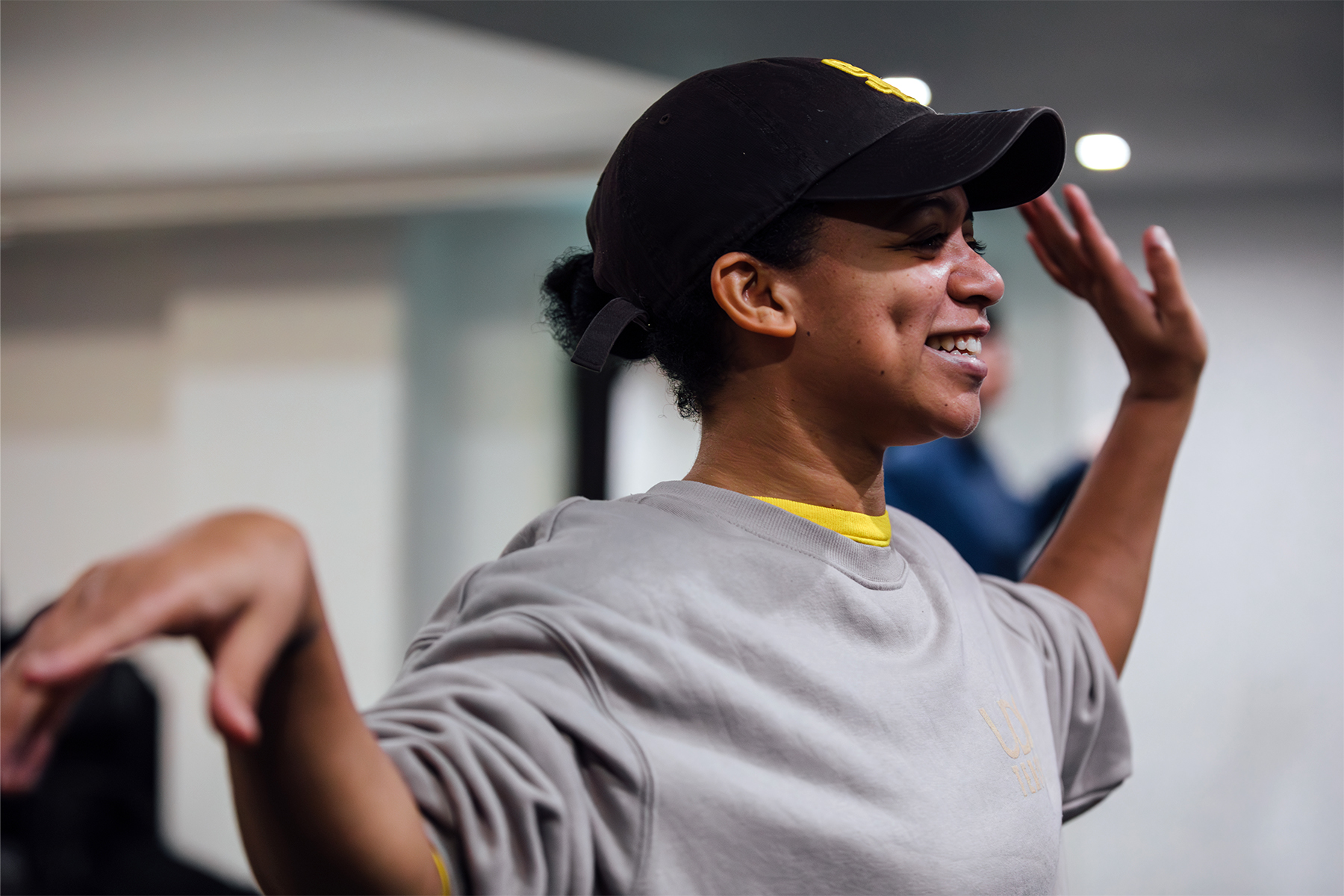 Aria, a black woman with dimples in sports gear smiles as she teaches vogue dance