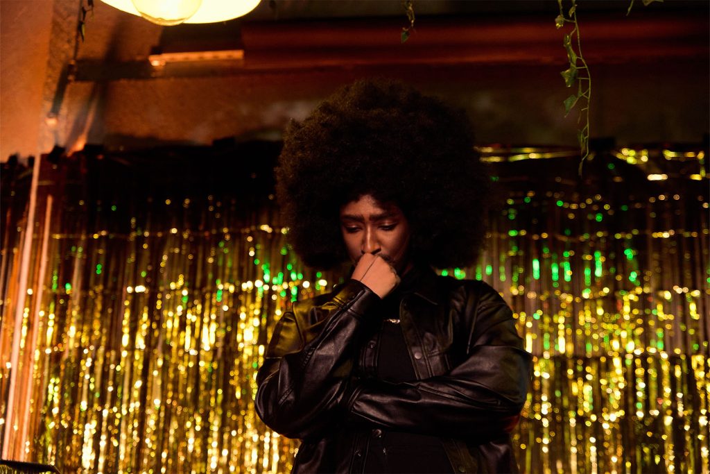 Unknown Amazon a black drag king with large afro stands contemplatively onstage