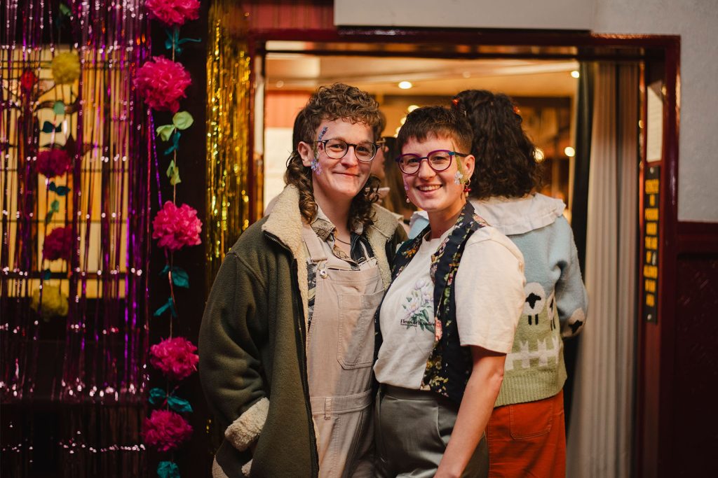 Two white queer people smile and wear spring themed floral clothing