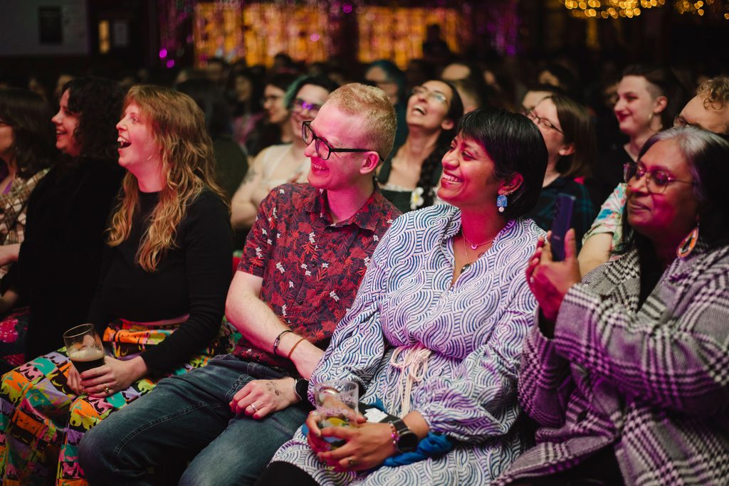 An audience smiles looking at the stage out of shot