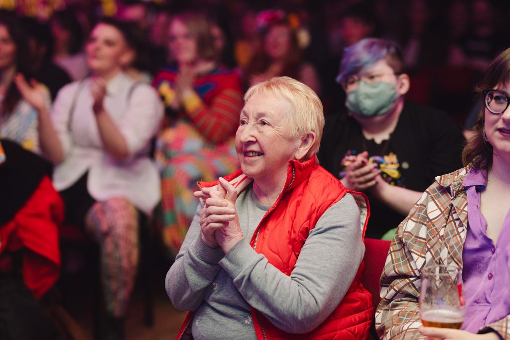 an older white woman smiles looking up at a stage out of shot