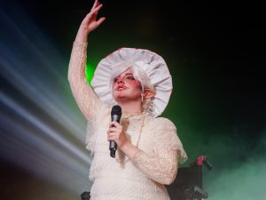 Drag king Pure Gliss sings dressed as a mushroom while onstage using a wheelchair